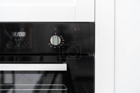 Téléchargez les photos : Detail on electric oven with glass door, knob button for choosing temperature mode and digital clock on display with icons, household appliance - en image libre de droit