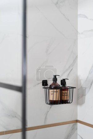 kompakter schwarzer Metallständer mit Duschgel und Körperlotion in braunen Flaschen an der Wand mit Marmorfliese im Badezimmer mit modernem Interieur