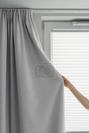 Foto de Tiro recortado de la cortina de tela gris de retención femenina y cerrar la ventana para proteger de la luz solar en el dormitorio con interior moderno, decoración casera - Imagen libre de derechos