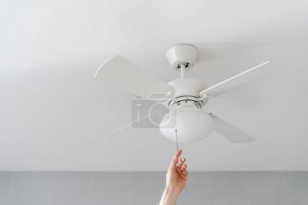 cropped shot of female hand pull switch of ceiling fan with lamp on white background with copy space, room cooling and ventilation concept