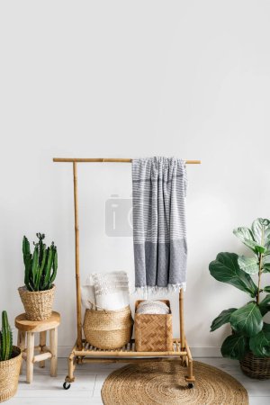 Photo for Detail in room with boho interior, plaid hanging on wooden clothes rack, pillows inside wicker basket, potted plants and round rug on floor, storage concept - Royalty Free Image