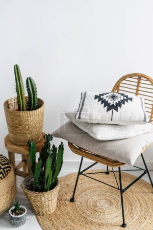 Photo for Home decor in interior with bohemian style, stack of cushions with pattern on rattan chair, houseplants in wicker pots and round rug - Royalty Free Image