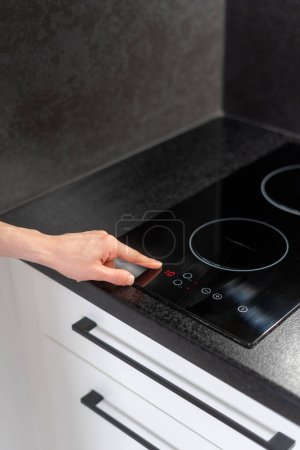 Photo for Cropped shot of female hand press button on glass ceramic induction hob and select temperature mode on control panel, modern household appliances concept - Royalty Free Image