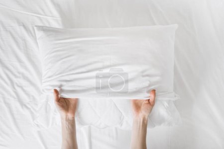 cropped shot of female hands putting fresh pillowcase on soft cushion on bed sheet background at home, make bed concept, housekeeping, top view