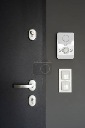 Foto de Vista de puerta cerrada con cerradura y mango de metal, interruptor de luz y puerta moderna con botón de control en la pared en el apartamento, sistema de intercomunicación inteligente - Imagen libre de derechos