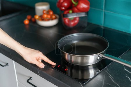 Foto de Tiro recortado de la mano femenina presiona el botón en el panel de control de la estufa de inducción y elegir la temperatura para cocinar en la sartén en la cocina casera - Imagen libre de derechos