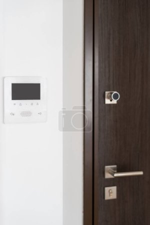 Photo for Vertical shot of video intercom gadget near the entrance wooden door. Control and protection device with buttons on white wall. Modern flat with security system - Royalty Free Image
