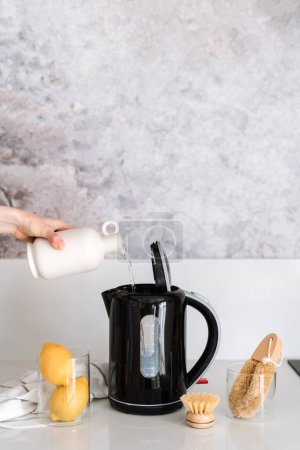 Photo for Descaling calcified black electric kettle with water, lemons and brushes on white top. Grey marble background. Housework problem and solution. - Royalty Free Image