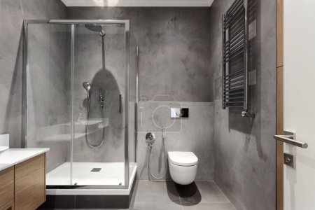 modernes Interieur im Hotelbad, Duschkabine mit Glastür, wandmontierte Toilette mit verstecktem Zisterne-Tank und beheiztem Edelstahl-Heizkörper