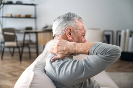 Photo for Elderly man rubbing hard pain in neck and massaging tense muscles. Feeling unwell, suffering from ache. Incorrect posture. Close up over shoulder view - Royalty Free Image