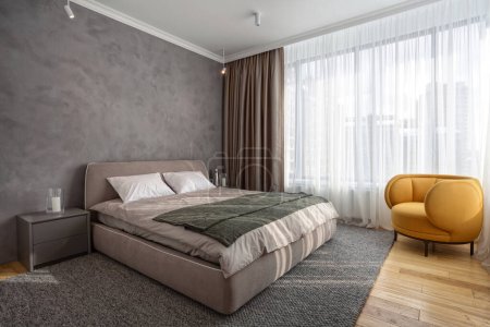 Photo for Light modern bedroom with comfortable furniture on natural wooden floor. Double bed on woven rug, close to bedside table and classic orange armchair. Concept of minimalist interior design in apartment - Royalty Free Image