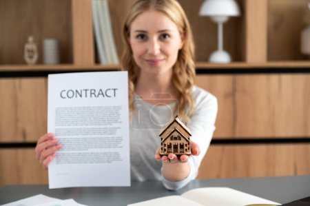 Selective focus on small wooden cottage house in female hand. Real estate agent prepare documents, contract for buying or selling building. Signing mortgage agreement in office