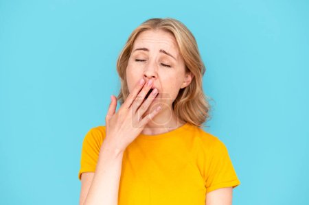 Photo for Tired woman with closed eyes yawning and covering mouth with hand over blue studio background. Feeling bored and sleep. Lack of energy concept. Need some relaxation - Royalty Free Image