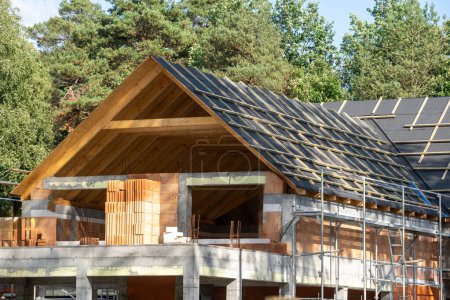 Häuserentwicklung. Gebäude im Bau. Prozess der Rekonstruktion, des Ersatzes und der Dacheindeckung. Holzdach mit wasserdichten Schutzschichten vor natürlichem Waldhintergrund