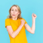 Optimistic and excited young woman in yellow t-shirt dancing isolated on blue copy space background. Concept of positive emotion. Happy overjoyed female raised fists up, moving on celebration party