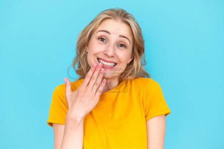 Woman with oops reaction isolated on blue background. Making mistake, fail, sorry. Happy and funny female overwhelmed by fake news, drama or secret with regret, shame or awkward