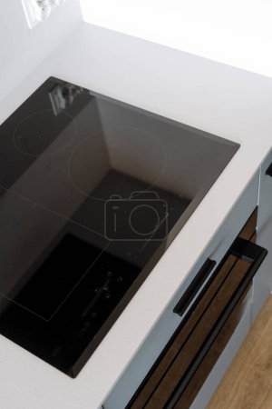 Hochwinkelaufnahme eines Induktionsherdes mit Bedienfeld und leerer, sauberer Glasoberfläche auf weißer Arbeitsplatte in einer Küche mit modernem Interieur. Integrierte Haushaltsgeräte zum Kochen zu Hause