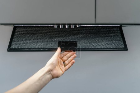 Cropped shot of woman hand taking aluminum mesh filter from extractor hood, replace or change dirty element for new and clean. Concept of easy maintenance household appliances