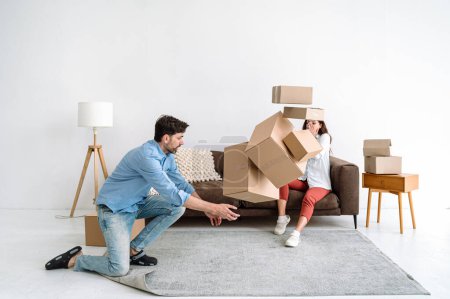 Photo for Adult man trying to catch cardboard boxes with personal staff falling on floor in living room. Moving to new apartment. Problem with balance. Woman worried about fragile things on cartons. - Royalty Free Image