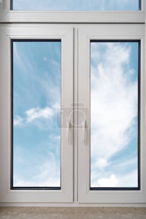 Foto de Tiro vertical de nueva ventana de doble acristalamiento de pvc de plástico cerrado con marco blanco instalado en la casa moderna. Vista al cielo azul con nubes. Conceptos publicitarios. Copiar espacio - Imagen libre de derechos