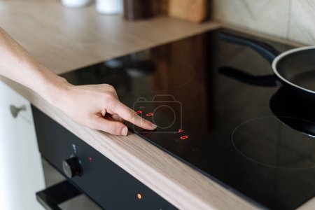 Selektiver Fokus auf die weibliche Hand drücken Taste auf dem digitalen Bedienfeld des Induktionsherds in der modernen Küche zu Hause. Weibliche Auswahltemperatur zum Kochen von Lebensmitteln auf sauberem Keramikherd.