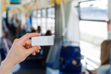 Enfoque selectivo en la mano del pasajero sosteniendo billete de papel contra el fondo interior borroso del transporte público. Es necesario pagar la tarifa en tranvía, tren. Copiar espacio