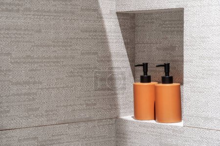 Aufbewahrung von Duschgel und Shampoo in Spenderflaschen in der Nische der gefliesten Wand im Badezimmer mit modernem minimalistischen Interieur. Kosmetikprodukte mit Kopierraum im heimischen Waschraum