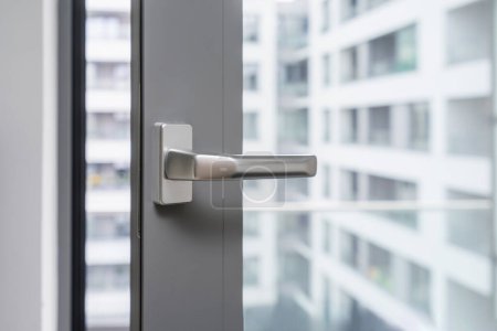 Closeup view of silver handle of opened gray pvc window against blurred office building background with copy space. Airing room. PVC metal and security profile.