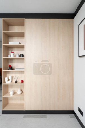 Wooden wardrobe with open shelves for keeping different things at living room. Modern closet with bookcase from wood material at stylish apartment with contemporary interior. Organized storage concept