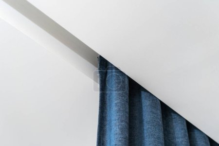 Close up of white ceiling board, curtain rail with blue textile in bedroom corner near light wall. Ideas for home decoration and design. Modern interior in apartment