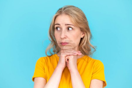 Studio portrait of young mistaken dissatisfied sad woman look aside on mock up area isolated on blue background. Lifestyle, shopping online concept