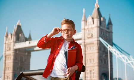 Photo for Student with backpack and books. Happy confident pupil ready for education in England. Portrait of boy with Tower bridge on background. Kid in glasses. English language courses. - Royalty Free Image