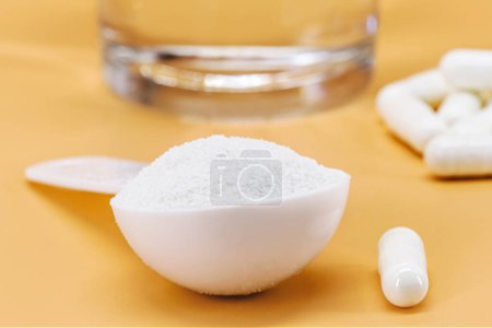 spoon of hydrolyzed collagen powder, and pills, with glass of water, protein for skin elasticity, isolated background and copyspace, macrophotography