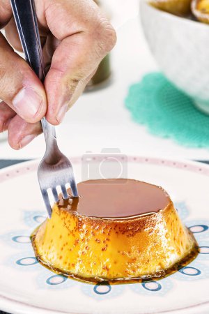 Téléchargez les photos : Hand with fork serving sweet condensed milk pudding, typical Brazilian dessert - en image libre de droit