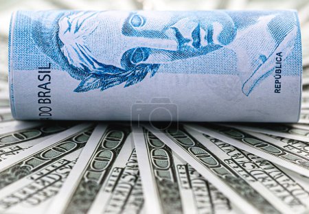 detail of one hundred reais bill surrounded by 100 dollar bills, concept of financial crisis between brazil and the united states