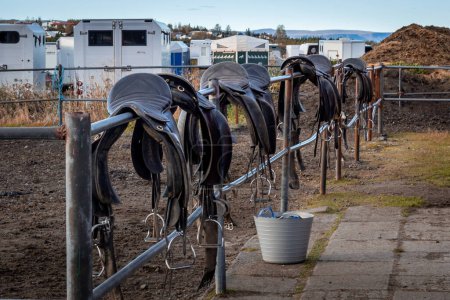 Téléchargez les photos : Selles de cheval suspendues en rangée sur la clôture de l'écurie. - en image libre de droit