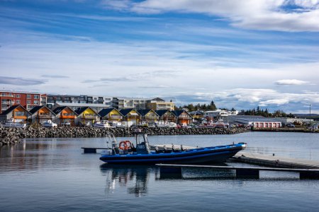 Photo for Reykjavik, Iceland - September 25, 2023: Blue dinghy boat moored in the Karsnes harbour, Kopavogur. Colorful cottages along the coastline in background. - Royalty Free Image