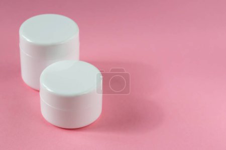 Two white cosmetic jars are standing on a pink background. Cosmetology, medicine, beauty, health and care