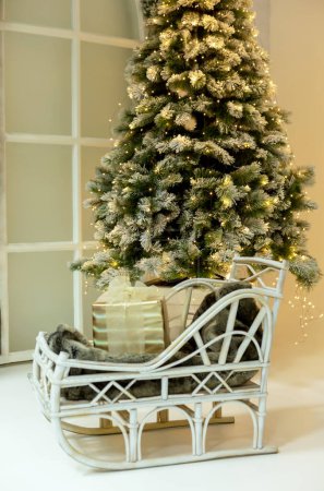 Photo for Christmas tree in lights in the interior. There is a sledge with a gift in front of it. New Year, Christmas, holidays. Selective focus, defocus - Royalty Free Image