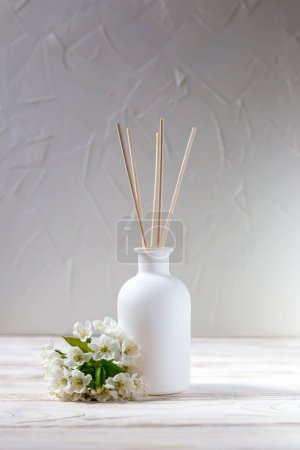 Foto de Perfume for the home. Aromatic reed diffuser and flowers in on a white background. The concept of tranquility, relaxation and enjoyment. Vertically - Imagen libre de derechos