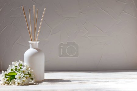 Foto de Perfume for home. Aromatic reed diffuser with sticks and flowers on a white wooden background in sunlight. The concept of tranquility, relaxation and enjoyment - Imagen libre de derechos