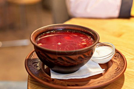 Partie copieux de bortsch classique dans un bol en argile sculptée avec de la crème sure dans un bol en verre, transmet une atmosphère chaleureuse de la cuisine d'Europe de l'Est sur fond en bois