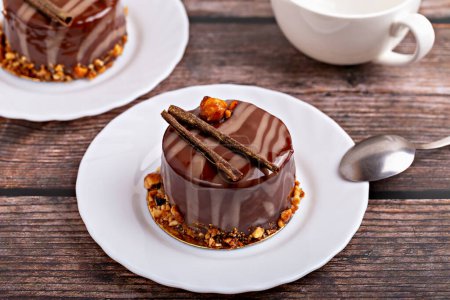 Frische leckere Schokoladenkuchen auf weißem Teller mit Löffel auf hölzernem Hintergrund. Karamellglasur und Dekoration verleihen Reiz und Lust