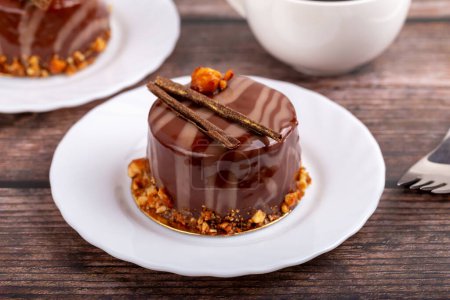 Frische leckere Schokoladenkuchen auf weißem Teller mit Gabel auf Holzgrund in Nahaufnahme. Karamellglasur und Dekoration verleihen Reiz und Lust
