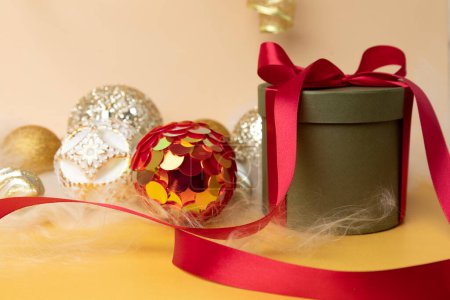 Foto de Año Nuevo y fondo de Navidad. Bolas de oro de Navidad y regalo redondo verde con cinta roja sobre un fondo amarillo con pelo de ángel. Vista frontal - Imagen libre de derechos