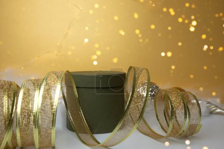Foto de Año Nuevo y fondo de Navidad. Cinta decorativa dorada y regalo redondo verde sobre fondo amarillo con pelo de ángel. Vista frontal - Imagen libre de derechos