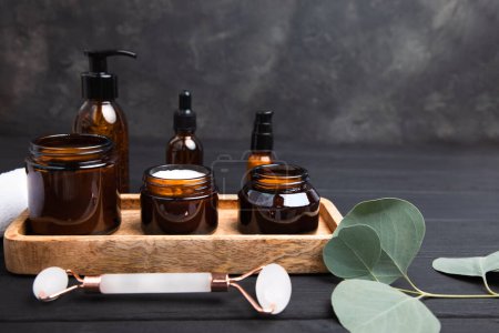 Amber bottles with facial cosmetics with a branch of eucalyptus on the dark wooden and concrete background. Front view