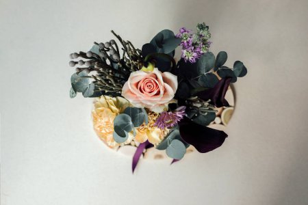 Ein Blumenstrauß in einem rechteckigen Paket auf grauem Betongrund. Strauß mit Rosen, Eukalyptuszweigen. Hintergrund mit Blumen. Ansicht von oben