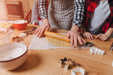 Foto de Papá e hijo en una mesa de madera en la cocina van a hacer galletas mediante el despliegue de la masa con un rodillo de madera. Vista superior - Imagen libre de derechos