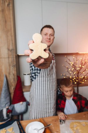 Foto de Papá e hijo en una mesa de madera en la cocina están haciendo galletas en la forma de poco humano. Vista frontal - Imagen libre de derechos